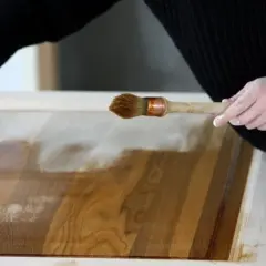 Mani che applicano vernice su un mobile in legno, mostrando come ristrutturare un mobile con cura e precisione.
