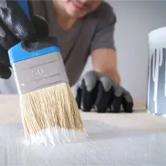 Mano guantata stende cementite bianca su una superficie di legno con un pennello.
