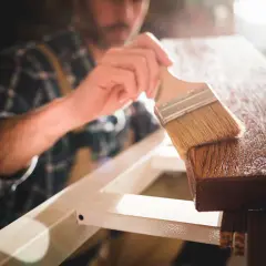 Un falegname applica una finitura su un pezzo di legno, esaltando le sue belle fibre del legno.