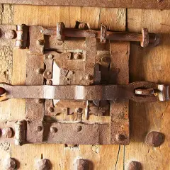 Parti di una serratura antica in ferro battuto su una porta di legno. I meccanismi arrugginiti suggeriscono una lunga storia.