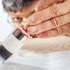 Un uomo applica il primer per legno con un pennello, preparando la superficie per la verniciatura.