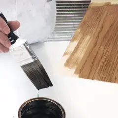 Pennello intinto in latta di impregnante, pronto per applicarlo su un campione di legno.
