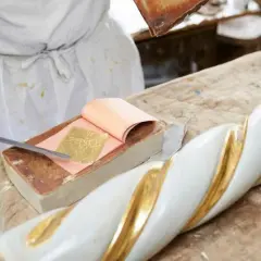 Artigiano applica foglia oro su un elemento decorativo bianco e oro. Scopri come si applica la foglia oro.