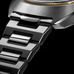 Dettaglio di un orologio con bracciale in metallo spazzolato e lucido. La corona nera presenta un logo inciso, un omaggio a un **singer reimagined**.