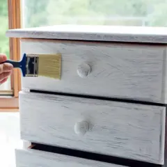 Restauro di un comò con chalk paint: un pennello applica la vernice per un look shabby chic.