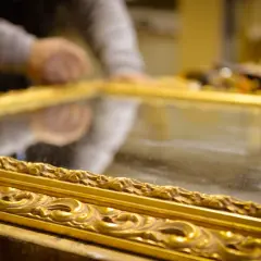 Mani esperte al lavoro per il restauro specchio antico. La cornice dorata e intarsiata riflette la cura del dettaglio.