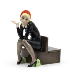 Figura in ceramica di donna con cappello rosso e abito nero, seduta su una panca. Un esempio per capire come riconoscere le bambole Lenci.