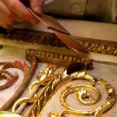 Mano applica una sottile foglia d'oro, una lega che imita l'oro, su un ornamento dorato e intagliato.