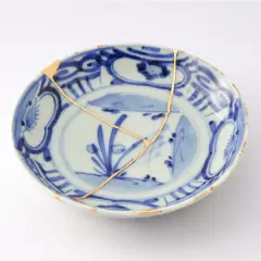 Piatto blu e bianco con crepe dorate, un esempio di tecnica del kintsugi che celebra la bellezza delle imperfezioni.