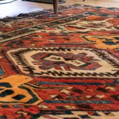 Tappeto persiano usato con motivi geometrici rossi, blu e gialli. Un pezzo d'antiquariato che conserva il suo valore.