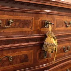 Dettaglio di mobili fine '800 con intarsi in noce e maniglie in bronzo. Un sacchetto decorativo pende da una serratura, testimoniando il loro valore storico.