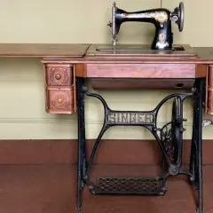 Macchina da cucire Singer d'epoca, con piano in legno e cassetti intagliati. Il suo valore storico la rende un pezzo da collezione.
