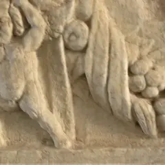 Dettaglio di un bassorilievo antico, forse parte di un restauro marmo, raffigurante figure mitologiche con drappeggi e grappoli d'uva.