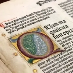 Dettaglio di antichi **primi libri stampati** con iniziale miniata e testo in latino.