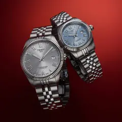 Due orologi Tissot con quadrante argentato e blu, entrambi con movimento automatico Powermatic 80, su sfondo rosso.