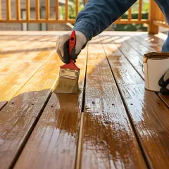 Persona con guanti applica una finitura protettiva su un deck di legno, mostrando come colorare il legno in modo naturale per un aspetto caldo e invitante.