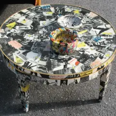 Tavolino rotondo con tecnica decoupage mobili, ricoperto di immagini in bianco e nero e fumetti colorati.