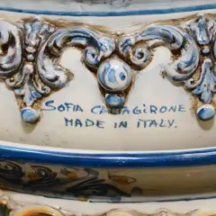 Dettaglio di un'opera in porcellana bianca e blu, con decorazioni barocche e la firma "Sofia Caltagirone Made in Italy".