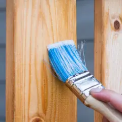 Pennello blu applica finitura a cera dopo impregnante su assi di legno.