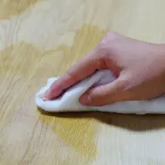 Mano che pulisce un tavolo di legno con un panno bianco, forse per sverniciare con soda caustica.