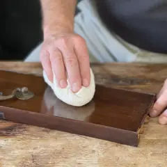 Mano lucida un mobile in legno con cera d'api, rivelando la sua bellezza naturale.