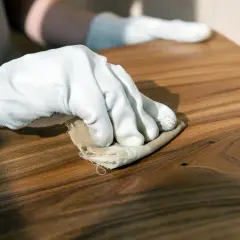Mano guantata lucida un mobile in legno con un panno, mostrando come usare la cera d'api per una finitura naturale e protettiva.