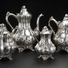 Un set di teiere e lattiera in argento antico, finemente cesellate con motivi floreali, un vero tesoro di grande valore.
