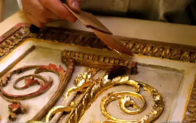 Mano applica una sottile foglia d'oro, una lega che imita l'oro, su un ornamento dorato e intagliato.