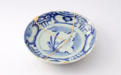 Piatto blu e bianco con crepe dorate, un esempio di tecnica del kintsugi che celebra la bellezza delle imperfezioni.