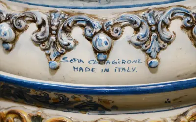 Dettaglio di un'opera in porcellana bianca e blu, con decorazioni barocche e la firma "Sofia Caltagirone Made in Italy".