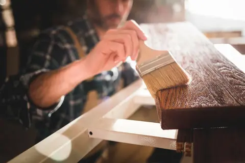 Un falegname applica una finitura su un pezzo di legno, esaltando le sue belle fibre del legno.