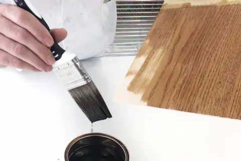 Pennello intinto in latta di impregnante, pronto per applicarlo su un campione di legno.