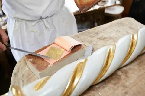 Artigiano applica foglia oro su un elemento decorativo bianco e oro. Scopri come si applica la foglia oro.