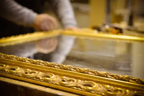 Mani esperte al lavoro per il restauro specchio antico. La cornice dorata e intarsiata riflette la cura del dettaglio.
