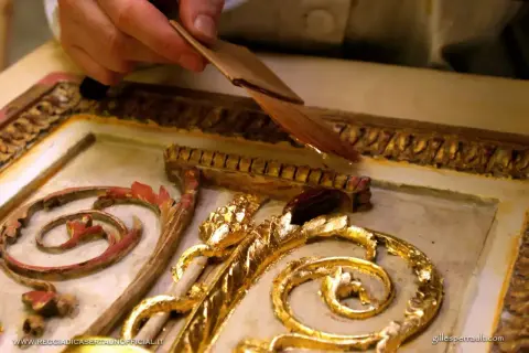 Mano applica una sottile foglia d'oro, una lega che imita l'oro, su un ornamento dorato e intagliato.