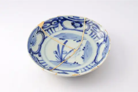 Piatto blu e bianco con crepe dorate, un esempio di tecnica del kintsugi che celebra la bellezza delle imperfezioni.