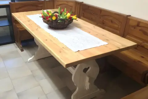 Tavolo in legno chiaro, pronto per essere lucidato, con un cestino di tulipani e una panca in legno scuro.