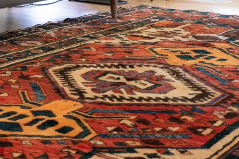 Tappeto persiano usato con motivi geometrici rossi, blu e gialli. Un pezzo d'antiquariato che conserva il suo valore.