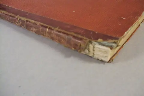 Dettaglio di una rilegatura libri vecchi con copertina rossa e dorso in pelle usurato, che mostra i segni del tempo.