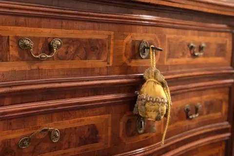 Dettaglio di mobili fine '800 con intarsi in noce e maniglie in bronzo. Un sacchetto decorativo pende da una serratura, testimoniando il loro valore storico.
