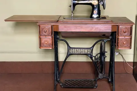 Macchina da cucire Singer d'epoca, con piano in legno e cassetti intagliati. Il suo valore storico la rende un pezzo da collezione.