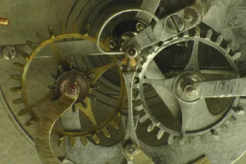 Ingranaggi dorati e argentati di un orologio, con un dettaglio dello scappamento coassiale che ne regola il movimento preciso.