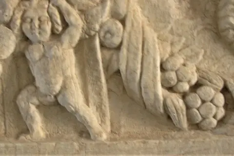 Dettaglio di un bassorilievo antico, forse parte di un restauro marmo, raffigurante figure mitologiche con drappeggi e grappoli d'uva.