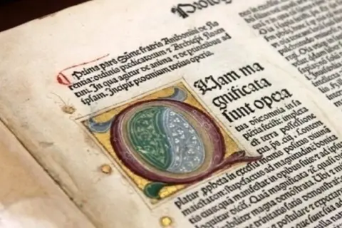 Dettaglio di antichi **primi libri stampati** con iniziale miniata e testo in latino.