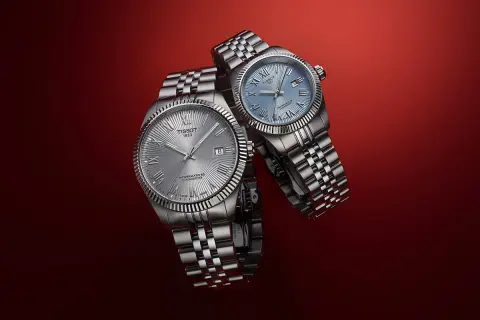 Due orologi Tissot con quadrante argentato e blu, entrambi con movimento automatico Powermatic 80, su sfondo rosso.