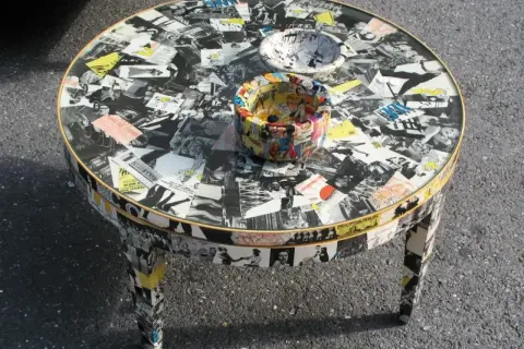 Tavolino rotondo con tecnica decoupage mobili, ricoperto di immagini in bianco e nero e fumetti colorati.