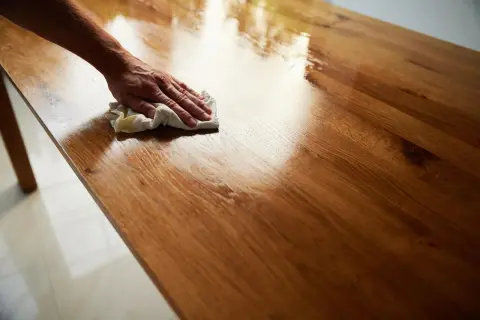 Mano che lucida un tavolo in legno con un panno, applicando una finitura a cera per un aspetto brillante e protetto.