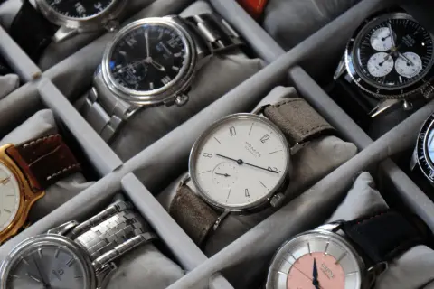 Collezione di orologi in un organizer. Un orologio al quarzo come funziona, con quadrante bianco e cinturino in pelle scamosciata, è in primo piano.
