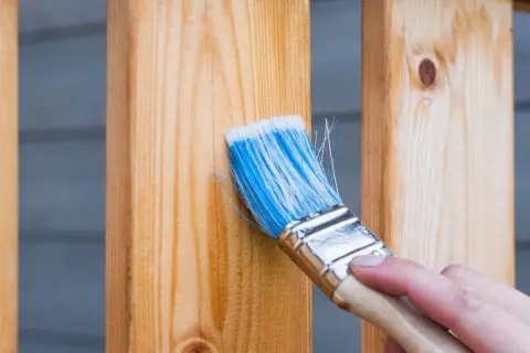 Pennello blu applica finitura a cera dopo impregnante su assi di legno.