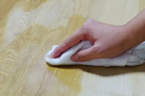 Mano che pulisce un tavolo di legno con un panno bianco, forse per sverniciare con soda caustica.
